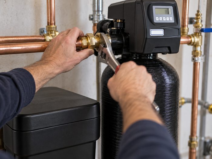 Technician's hands installing a water softener with a wrench, copper piping visible